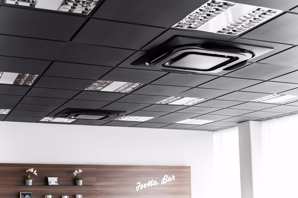 Černé kazetové jednotky Daikin zapuštěné do tmavého kazetového podhledu v zázemí